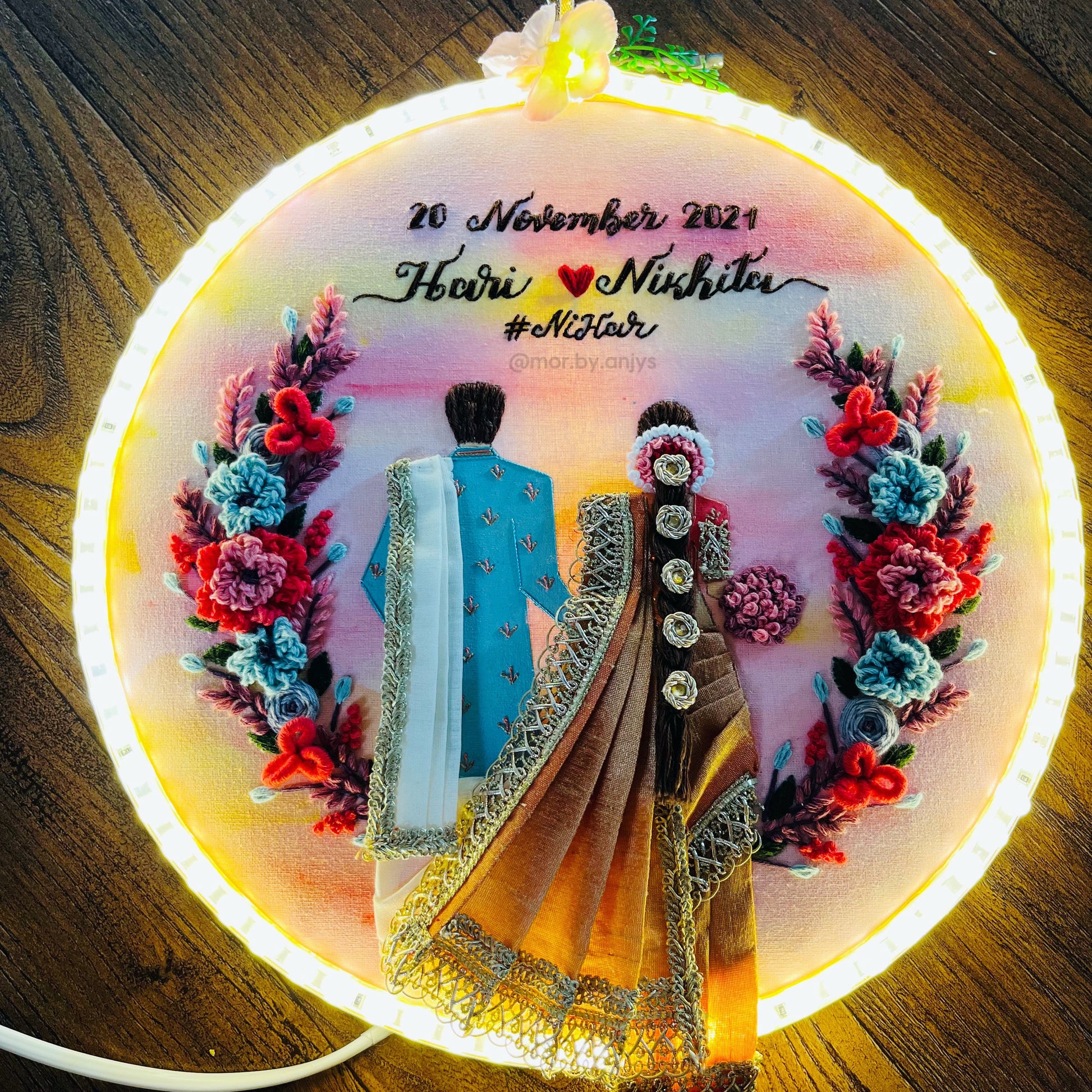 Decorative embroidery hoop with a couple in traditional attire and floral design, illuminated from within.