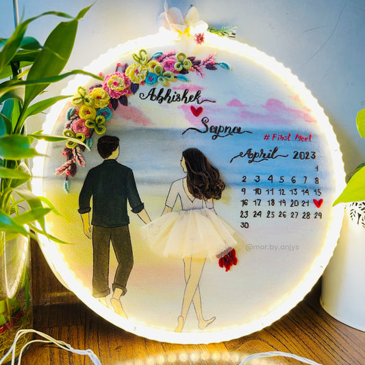 Decorative calendar with illustration of a couple and floral design, surrounded by plants and fairy lights.