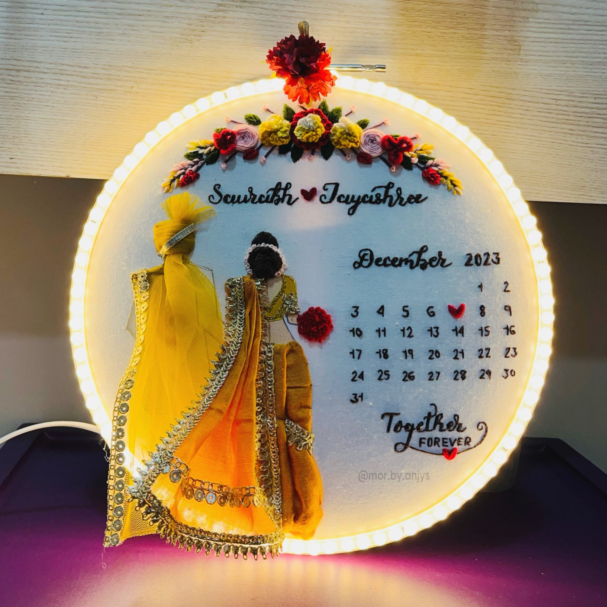 Decorative calendar with illustrated couple and LED lighting on a dark surface.