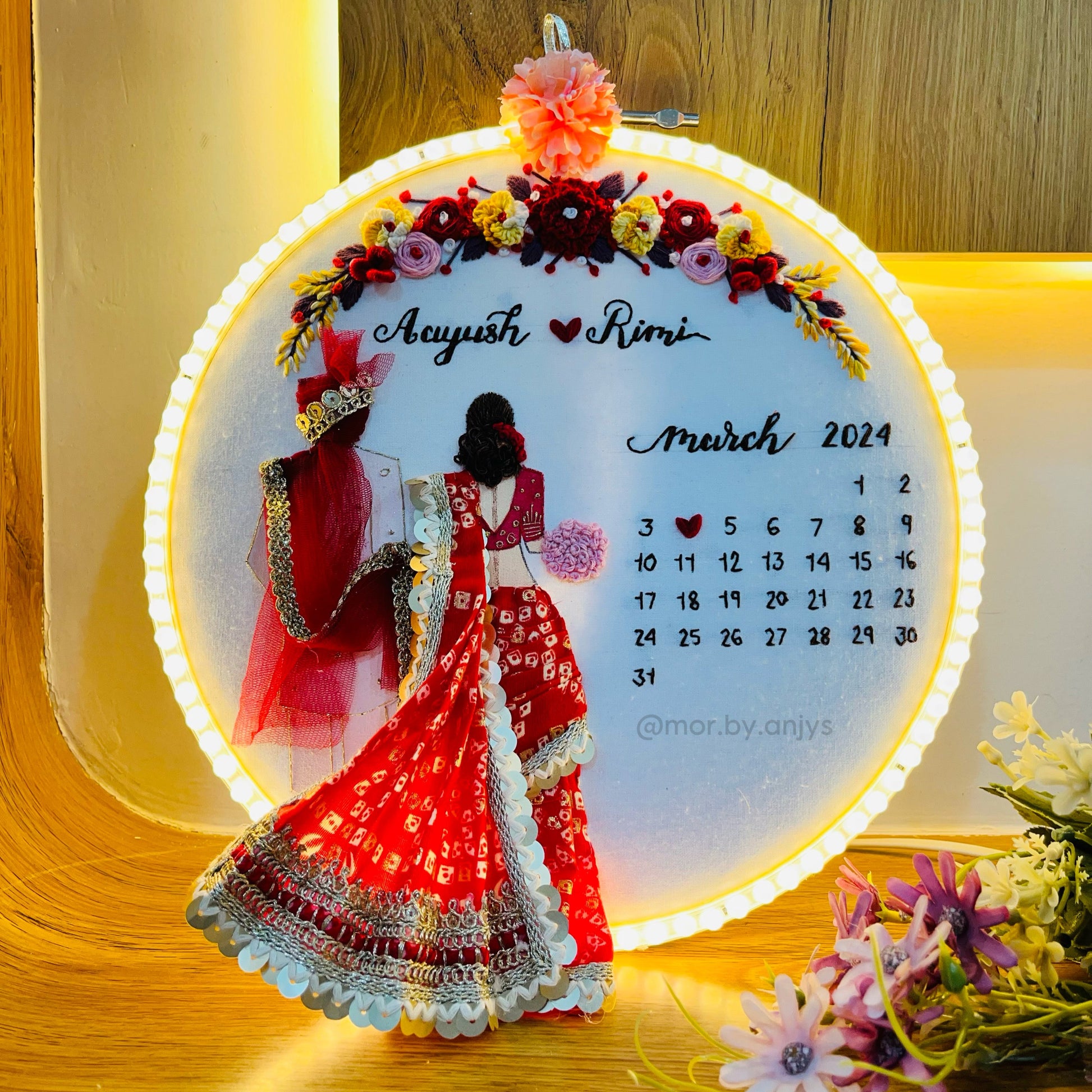 Decorative calendar with a couple in traditional attire and floral design, placed on a wooden surface.
