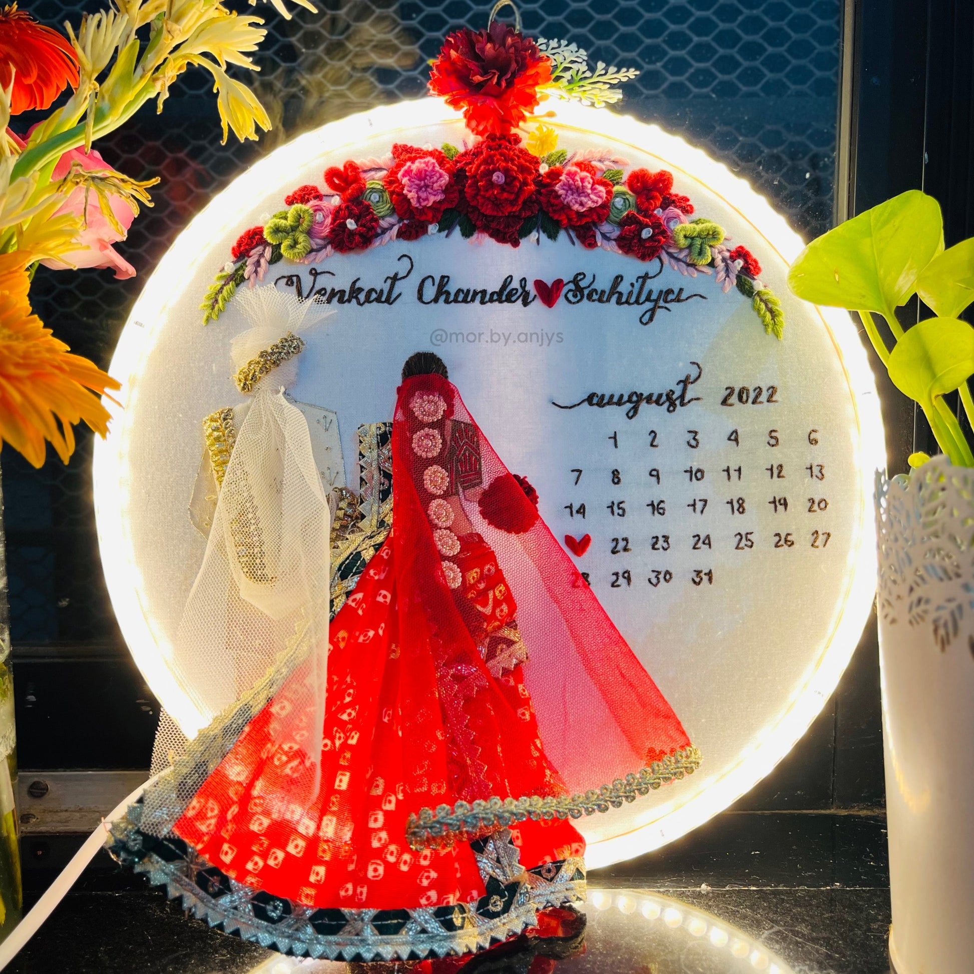 Decorative calendar with a woman in a red outfit and floral design, surrounded by flowers and plants.