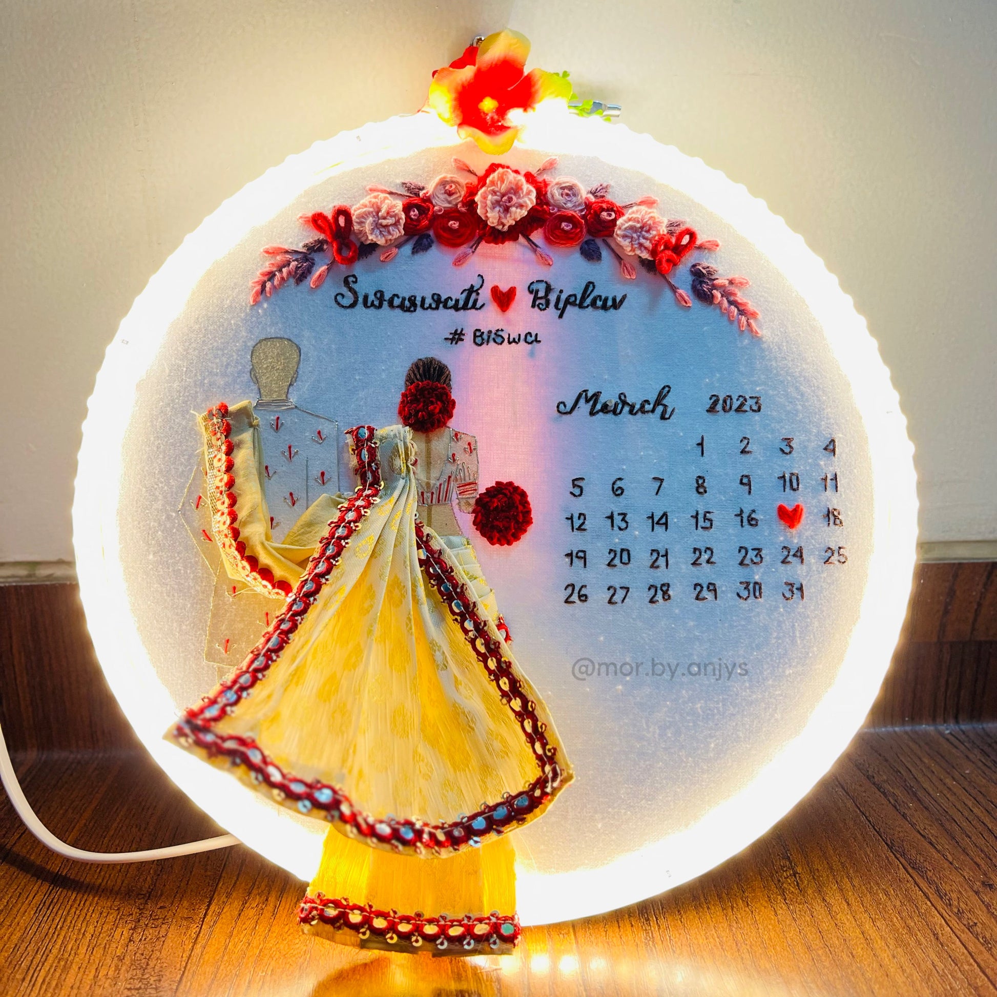 Decorative calendar with illuminated base featuring a couple and floral design on a wooden surface.