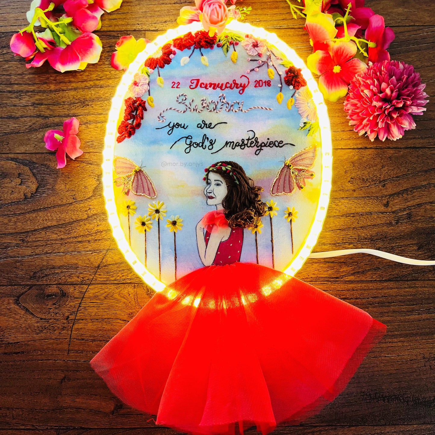 Decorative LED sign with floral design and text on a wooden surface