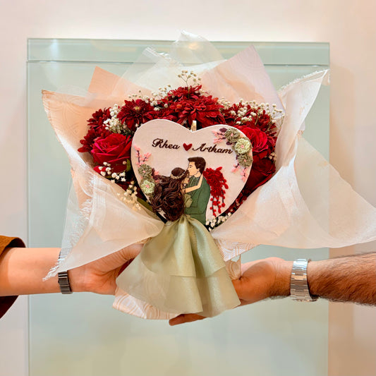 Bouquet of red roses with a heart-shaped card held by two people.