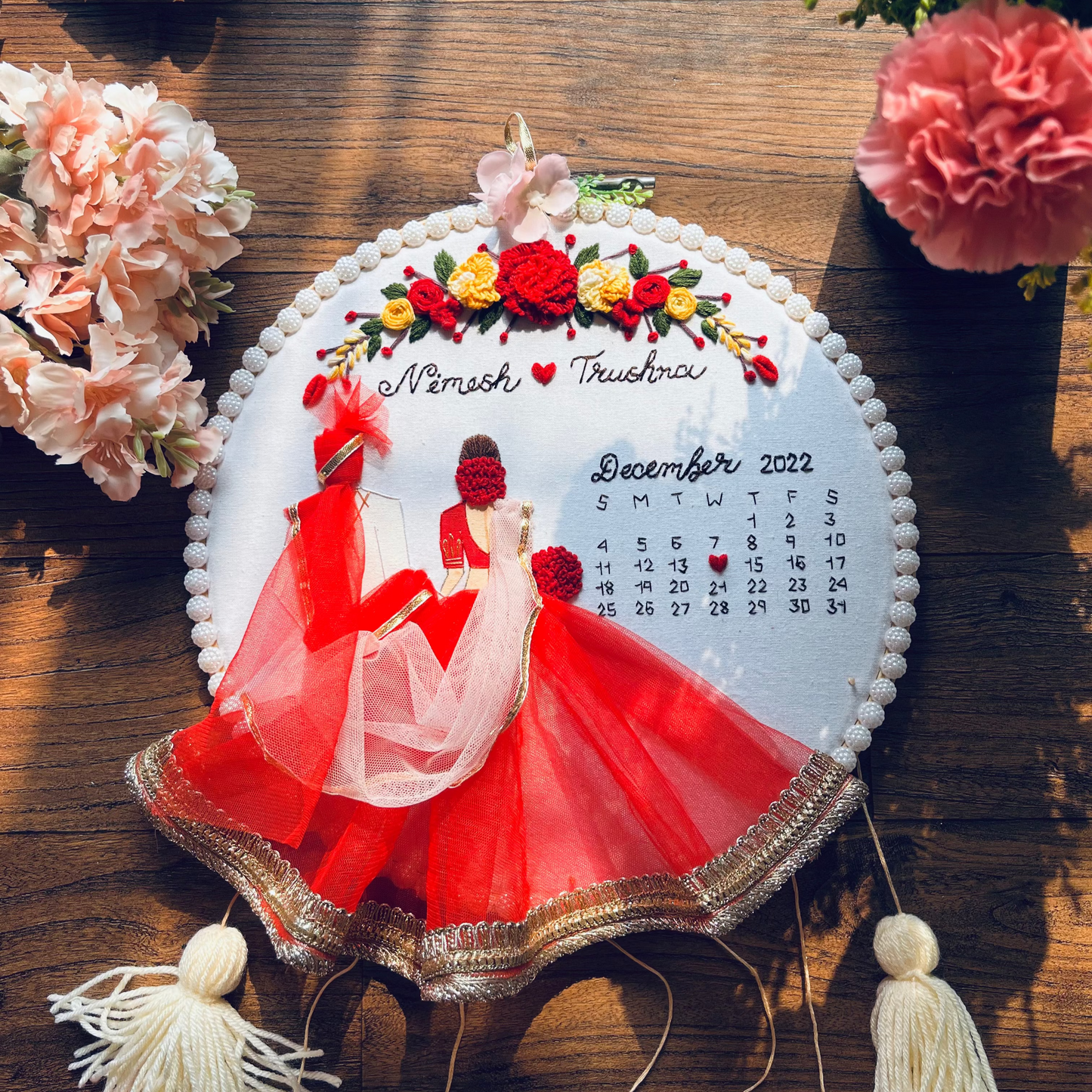 Decorative calendar with a couple in red on a wooden surface with flowers.